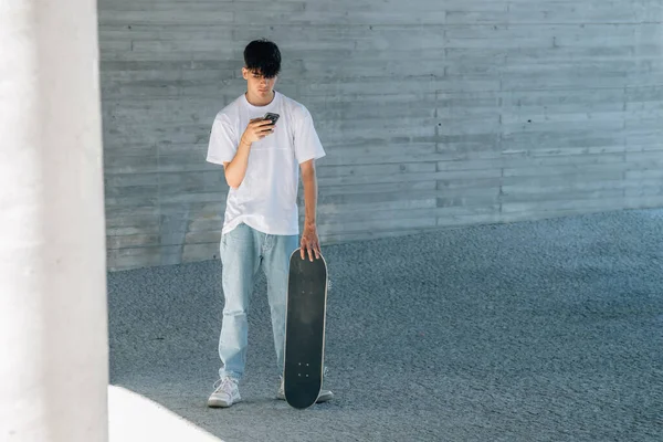 市内に携帯電話とスケートボードを持っている若い男 — ストック写真