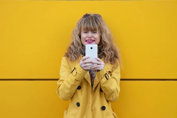通りの黄色い壁に携帯電話を持った女性が — ストック写真