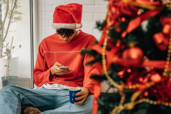クリスマスのために家に携帯電話を持っている若い男 — ストック写真