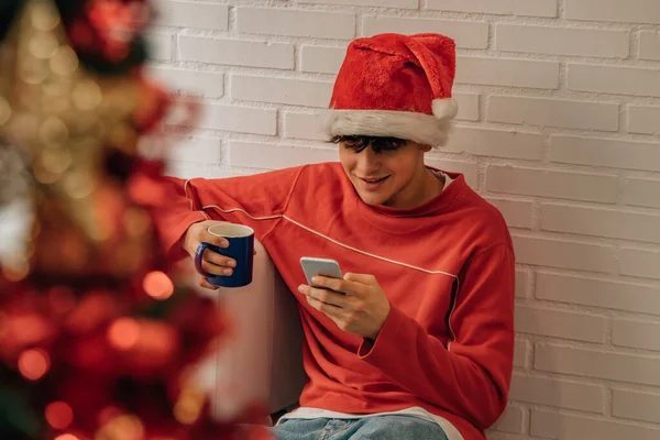 十代の男の子とともに携帯電話とサンタ クラスの帽子自宅でクリスマス — ストック写真