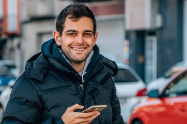 Kışlık ceketli ve cep telefonlu bir adam sokakta.