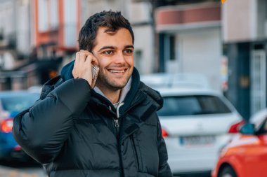 Kışlık ceketli bir adam cep telefonuyla konuşuyor.