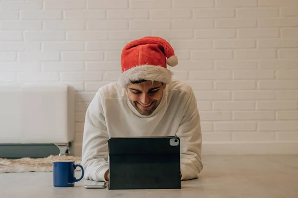 サンタ クラスの帽子とコンピューターを手にクリスマスに家にいる男 — ストック写真