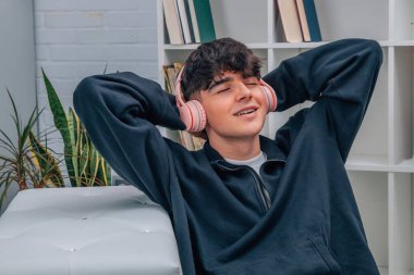 Genç adam evde kulaklıkla müzik dinliyor.