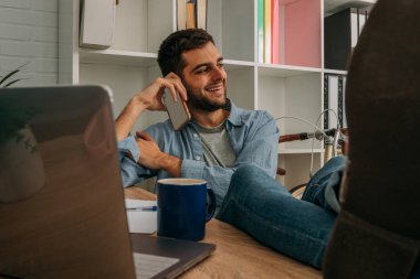 Evdeki ya da ofisteki bir adam ayaklarını masaya koyup rahatça cep telefonuyla konuşuyor.