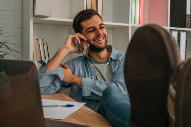 Evdeki ya da ofisteki bir adam ayaklarını masaya koyup rahatça cep telefonuyla konuşuyor.