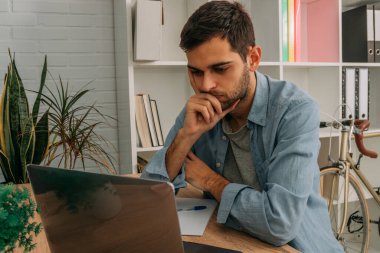 Evde bilgisayar başında düşünceli ya da karar veren bir adam var.