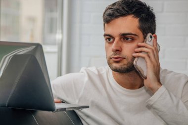 Cep telefonu ve bilgisayarı olan bir adam evde.