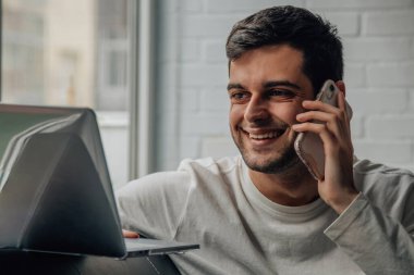 Cep telefonu ve bilgisayarı olan bir adam evde.