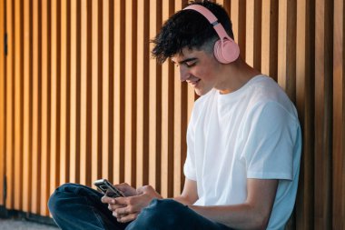 Sokakta cep telefonu, akıllı telefon ve kulaklığı olan genç bir adam.