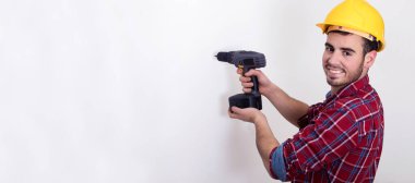 Duvarcı beyaz duvarda kask ve matkapla çalışıyor.