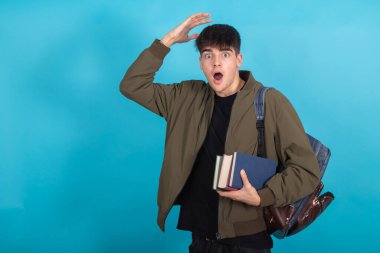 Sırt çantalı ve kitaplı öğrenci mavi arka planda izole edilmiş.