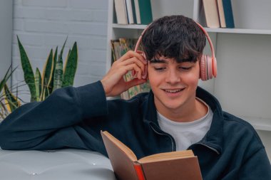 Genç adam evde kitap okuyor ve kulaklıkla müzik dinliyor.
