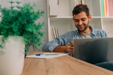 Adam evde dizüstü bilgisayar ve cep telefonu, cep telefonu veya akıllı telefon ile çalışıyor.