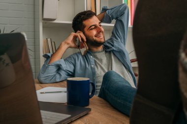 Evdeki adam cep telefonuyla konuşan bilgisayarla rahatlamış.