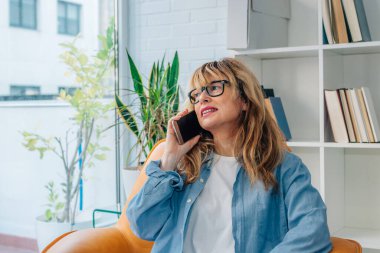 Kadın evde cep ya da cep telefonuyla konuşuyor.