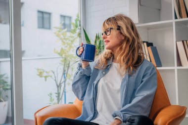 Bir fincan kahve ya da içkiyle evde bir kadın var.