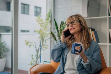 Kadın evde cep ya da cep telefonuyla konuşuyor.