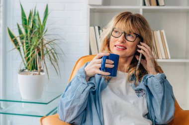 Orta yaşlı bir kadın evde cep telefonuyla mı konuşuyor yoksa bir fincan kahveyle mi konuşuyor?