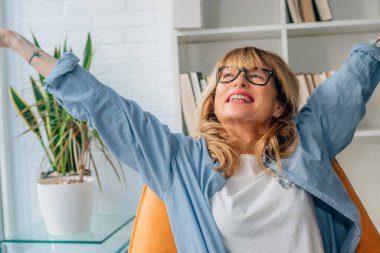 Orta yaşlı bir kadın kollarını kaldırmış mutlu mesut eğleniyor.