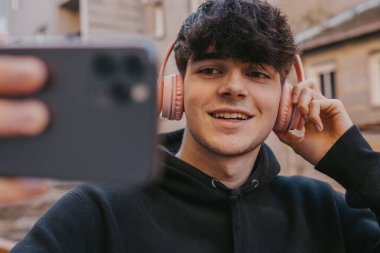 Cep telefonu ve kulaklığı olan genç adam fotoğraf çekiyor.