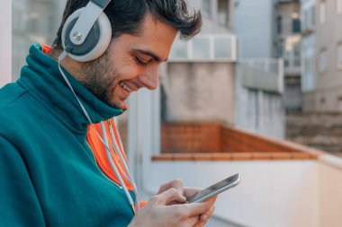 Sokakta cep telefonu ve kulaklığı olan genç bir adam.