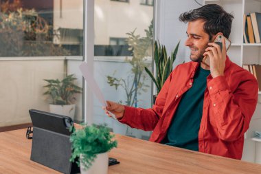 Evde çalışan ve cep telefonuyla konuşan bir adam.