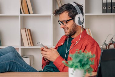 young man at home with mobile phone and headphones listening to music