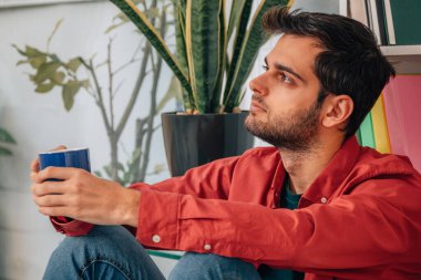 Evde bir fincan kahveyle düşünceli bir adam.