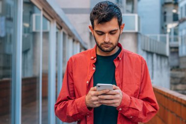 Sokakta cep telefonu olan kırmızı gömlekli sıradan bir adam.