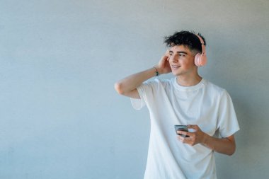 Cep telefonu ve kulaklığı olan genç bir çocuk duvarda kopyalanmış bir şekilde müzik dinliyor.