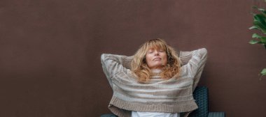 Orta yaşlı bir kadın teras kanepesinde dinleniyor.