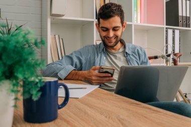 Adam evde dizüstü bilgisayar ve cep telefonu, cep telefonu veya akıllı telefon ile çalışıyor.