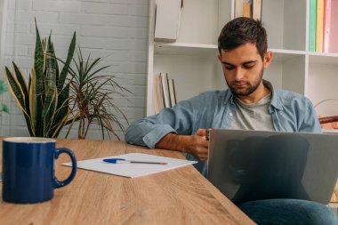 Adam evde dizüstü bilgisayar ve cep telefonu, cep telefonu veya akıllı telefon ile çalışıyor.