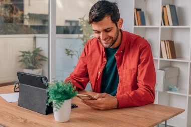 Bilgisayarı ve cep telefonu olan genç bir adam.