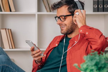 Evde cep telefonu ve kulaklığı olan bir adam var.