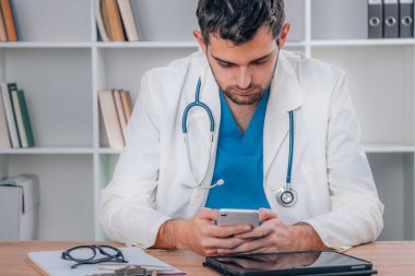 Üniformalı genç doktor ve cep telefonlu steteskop.