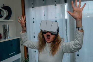 Evde sanal gerçeklik gözlüklü bir kadın metaevrenin tadını çıkarıyor.