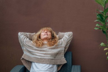 Orta yaşlı bir kadın teras kanepesinde dinleniyor.
