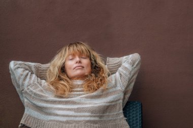 Orta yaşlı bir kadın teras kanepesinde dinleniyor.