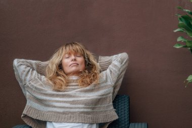 Orta yaşlı bir kadın teras kanepesinde dinleniyor.