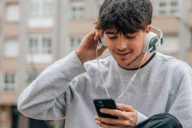 Şehirde kulaklığı ve cep telefonu olan genç bir çocuk.