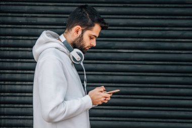 Genç adam cep telefonu ve kulaklıkla yürüyor.