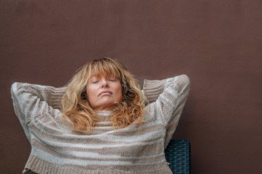 Orta yaşlı bir kadın teras kanepesinde dinleniyor.