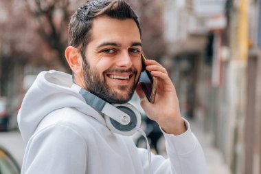 Genç adam sokakta cep veya cep telefonuyla konuşuyor.