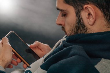 Evdeki koltukta oturan adam cep telefonuna bakıyor.