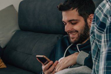 Evdeki koltukta oturan adam cep telefonuna bakıyor.