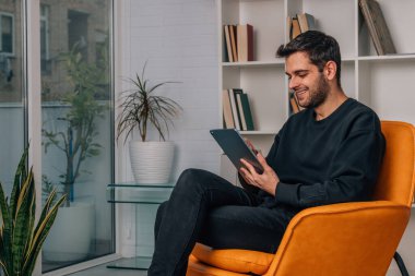 Genç adam evde dijital tablet veya dizüstü bilgisayar kullanıyor