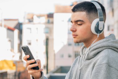 Kulaklıklı ve cep telefonlu genç adam sokakta müzik dinliyor.