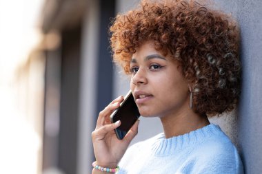Afro-Amerikalı kız sokakta telefonla konuşuyor.